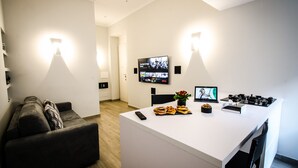 Ein zeitgemäßer Wohnraum mit Kücheninsel, einem Wand-Fernseher und einer Essecke mit Laptop und Pizza.