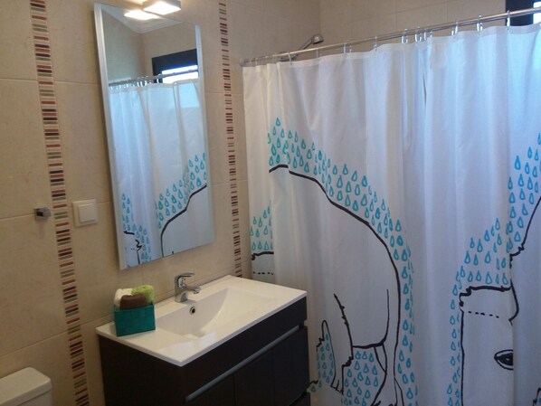Une salle de bain avec un lavabo blanc, des meubles sombres, un miroir et un rideau de douche orné d’un motif de gouttes de pluie.
