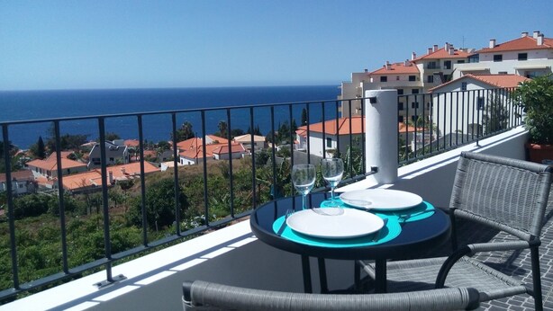 A balcony with a table set for two, overlooking a coastal town and the sea. - Sidewalk Cottage (Caniço)