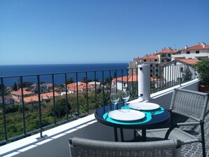 Un balcon avec une table dressée pour deux personnes, offrant une vue sur une ville côtière et la mer.
