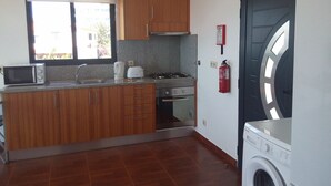 A compact kitchen with wooden cabinets, a microwave, a toaster, and a gas stove. - Sidewalk Cottage (Caniço)