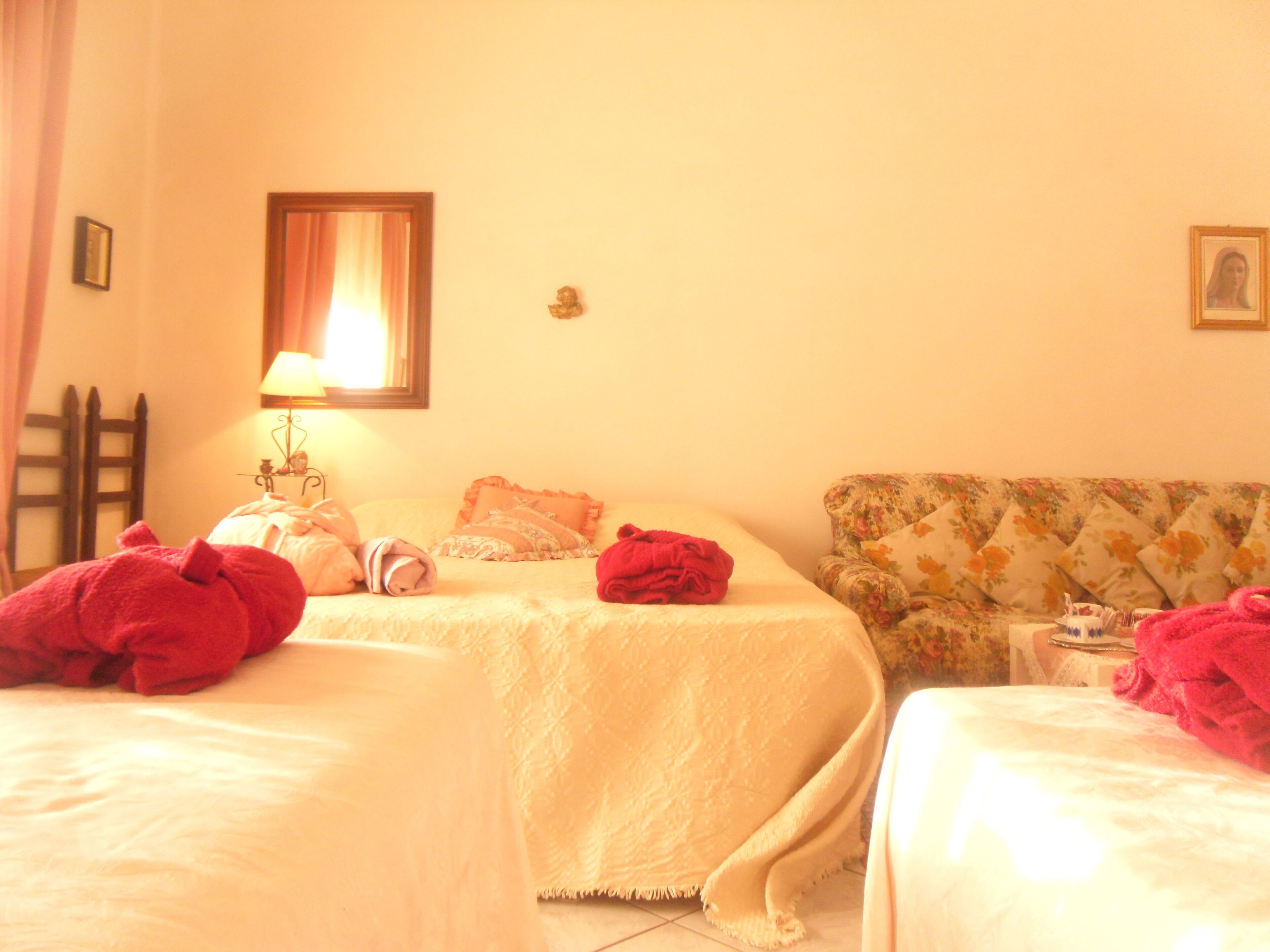Ein Hotelzimmer mit zwei Betten, einem Nachttisch, einer Lampe und einem blumigen Sofa.