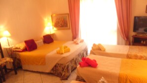 A hotel room with two beds, a small table with a lamp, a television, and a painting on the wall.