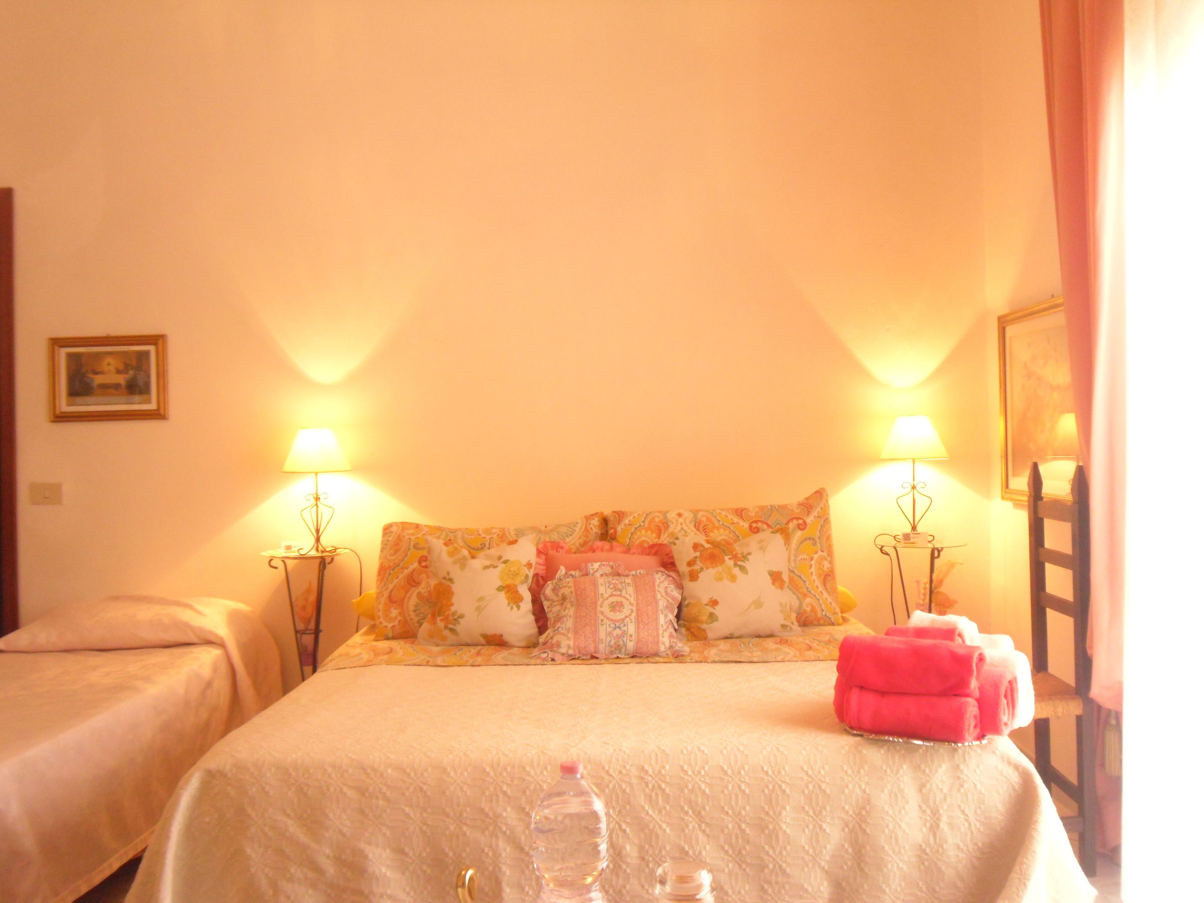 Une chambre d’hôtel avec deux lits, chacun étant agrémenté d’une table de chevet et d’une lampe assorties. Une bouteille d’eau se trouve sur le lit et une serviette pliée sur la table de chevet.