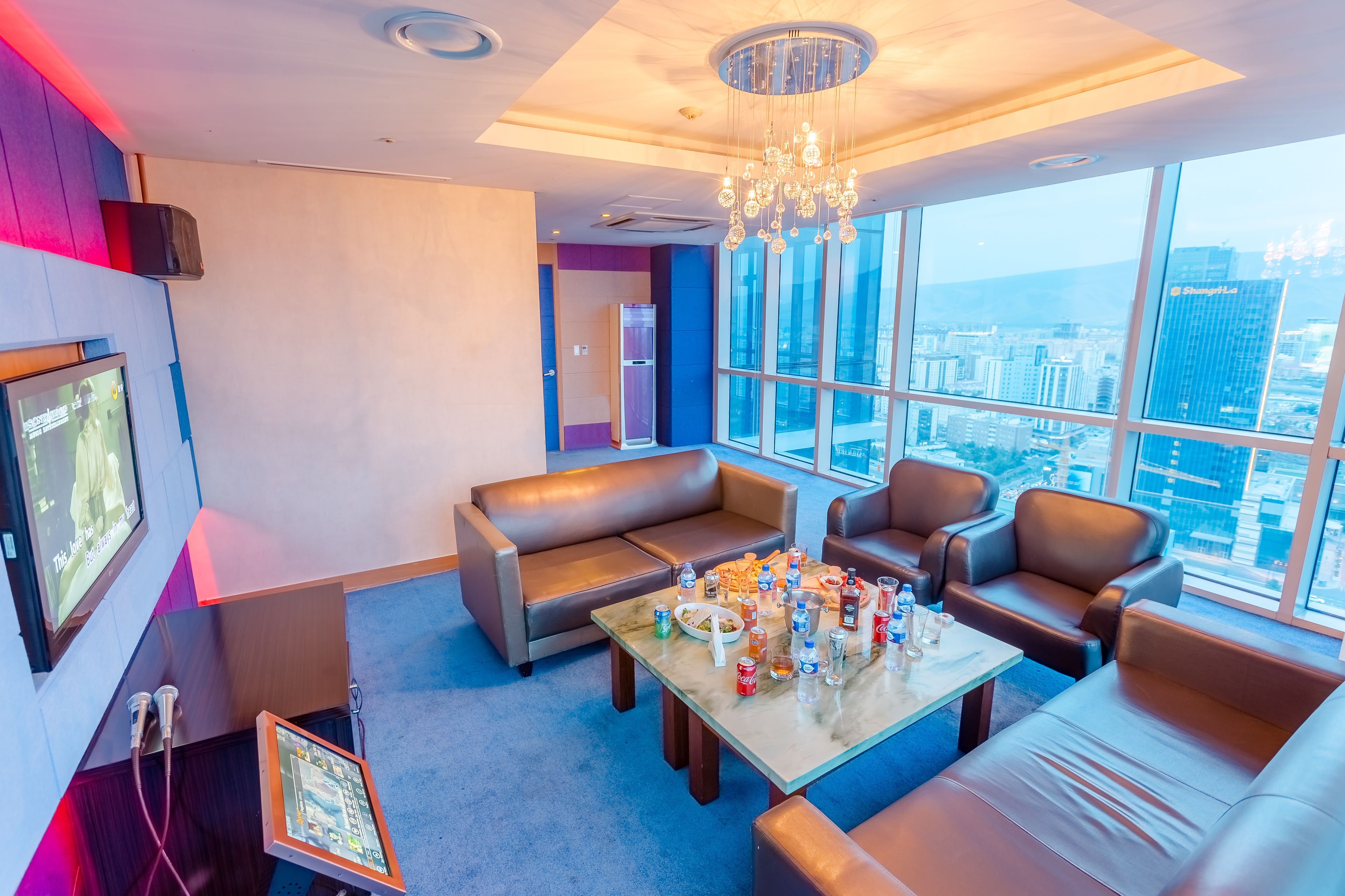 Una habitación de hotel moderna con un ventanal amplio que ofrece vistas a la ciudad, un área de descanso cómoda con una mesa dispuesta para comer, y un televisor en la pared.