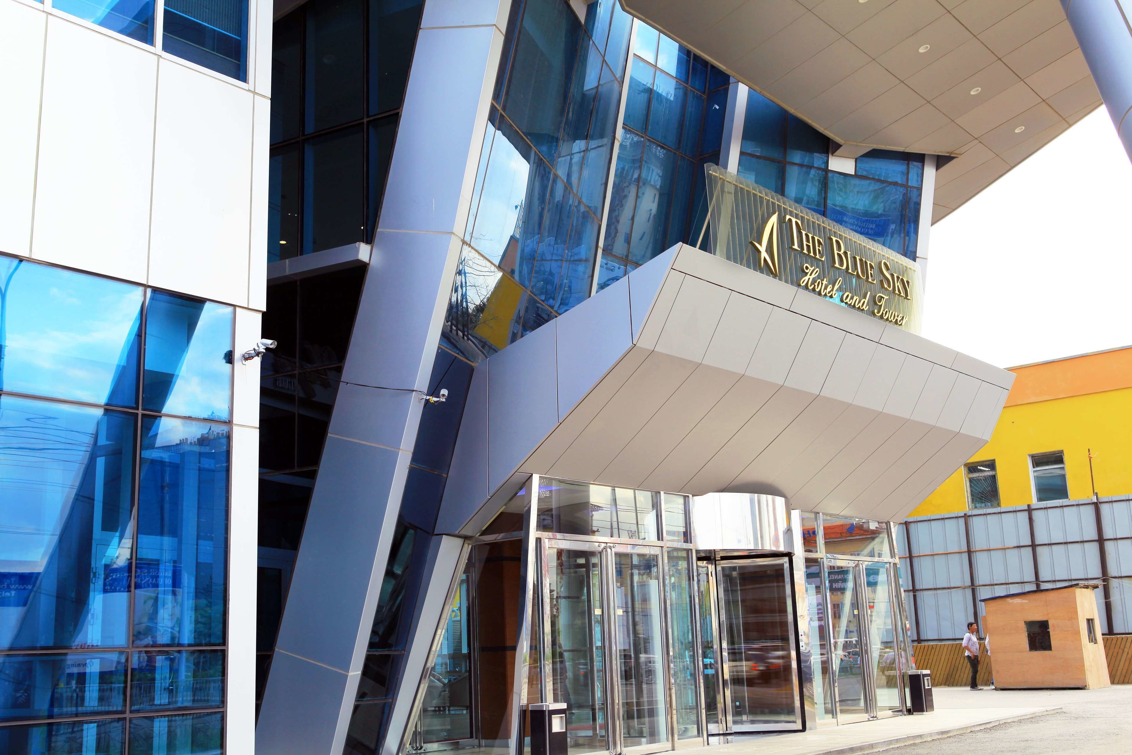A modern hotel with a glass facade and a sign reading "The Blue Sky Hotel and Tower."