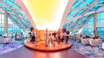 A modern hotel lobby with a stage for live music, seating areas, and large windows offering city views.