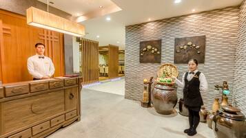 A reception area with a wooden counter, a receptionist, and a wall decorated with pottery and a stone wall.