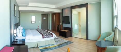 Een moderne hotelkamer met een bed, zithoek, televisie en een glazen deur naar een badkamer.