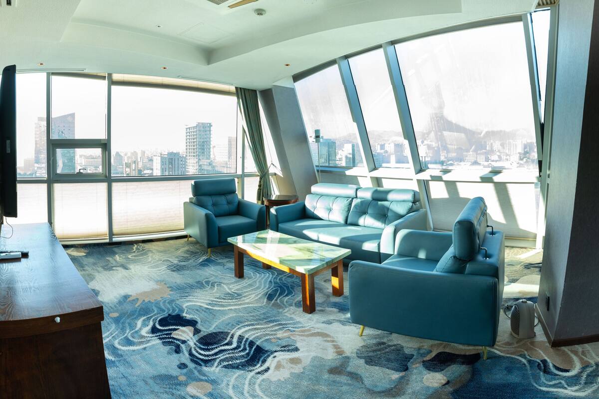 Una sala de estar moderna con un ventanal grande, un sofá azul, una mesa de centro de madera y una alfombra estampada.