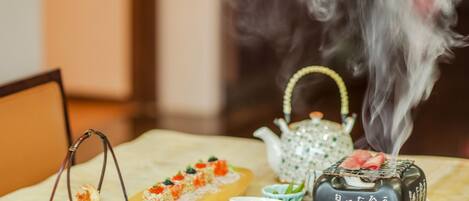 Una mesa dispuesta con diversos platos, una tetera y un pequeño quemador de incienso que emite humo.