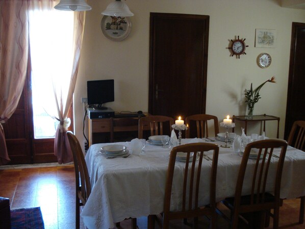 A dining room with a table set for four, two candles, a computer on a desk, and a clock on the wall. - VILLA WITH LARGE TERRACES AND GARDENS WITH SEA VIEW (SCIACCA)