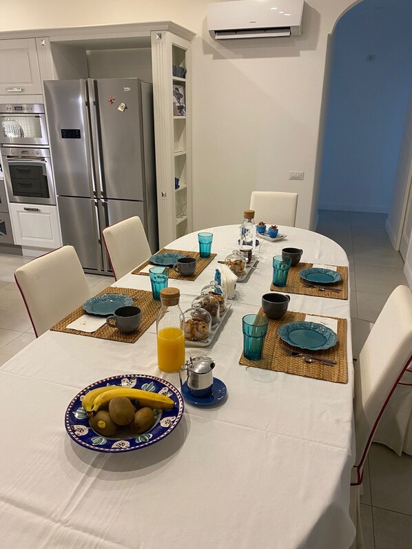 A dining area with a white table set for breakfast, including plates, cups, and a fruit bowl.