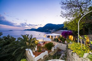 A coastal property with a patio overlooking the sea, stone walls, and tropical plants.