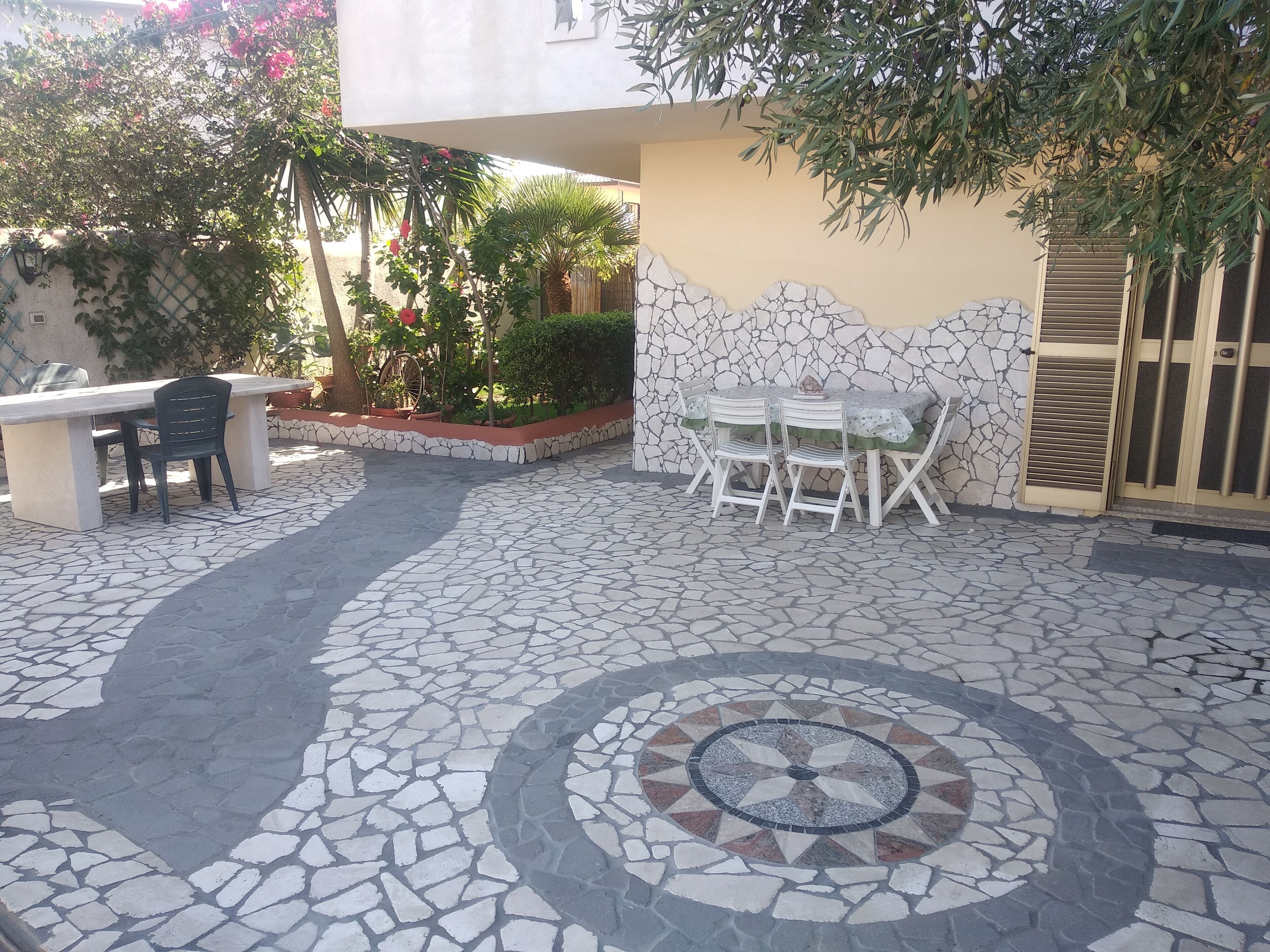 Un patio con piso de baldosas de piedra, una mesa de comedor con sillas y un pequeño rincón de estar con un banco y sillas.