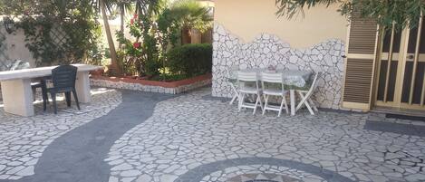 Un patio con piso de baldosas de piedra, una mesa de comedor con sillas y un pequeño rincón de estar con un banco y sillas.