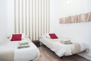 Ett hotellrum med två separata sängar, var och en med en röd kudde och en hopvikt handduk. Rummet har en randig vägg och ett trägolv.