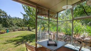 Une véranda avec une table et des chaises, entourée d’un mur de pierre et d’une végétation luxuriante.