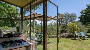 Une cuisine équipée d’une cuisinière à gaz, d’un évier et d’une fenêtre donnant sur un jardin où se trouvent un hamac, des chaises et une table.