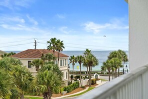 A coastal view with a house, palm trees, and a clear sky.