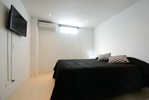 A bedroom with a bed, a television, an air conditioning unit, and a window.