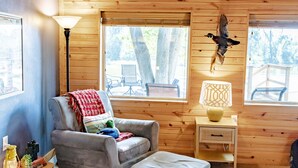 L’intérieur d’un chalet accueillant, avec un plafond en bois, un fauteuil gris agrémenté d’une couverture rouge, une lampe et une sculpture d’oiseau fixée au mur.