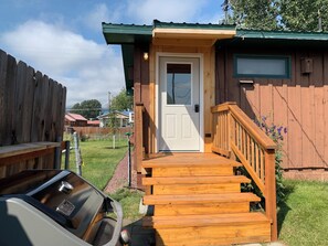 Una cabaña de madera con puerta principal, escalera de madera y un pequeño porche.