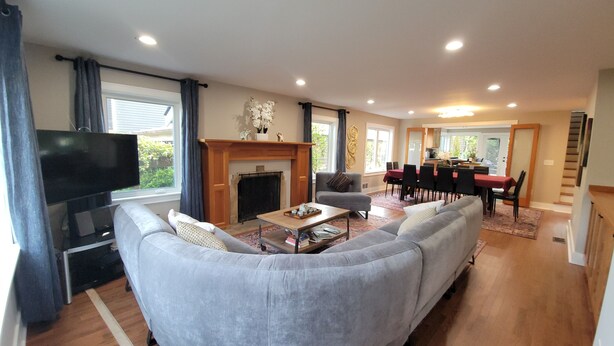 A living room with a large grey sofa, a flat-screen TV, a fireplace, and a dining area with a red tablecloth. - Gorgeous Huge 6-8BR Heart of Seattle—One Block from Lake (Seattle)