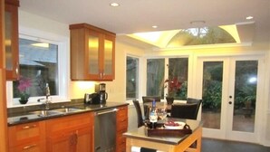 A modern kitchen with wooden cabinets, a built-in dishwasher, and a dining area with a table and chairs. - Gorgeous Huge 6-8BR Heart of Seattle—One Block from Lake (Seattle)