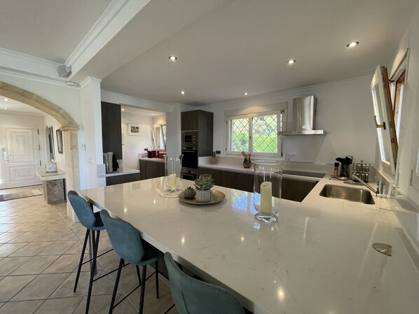 A modern kitchen with a large island, bar stools, a window with a view, and built-in appliances.