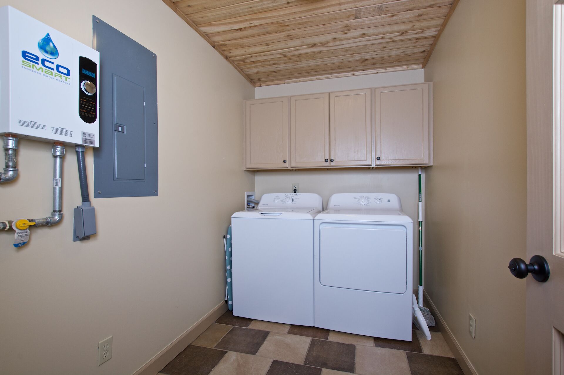 A laundry room with two washing machines, a water heater, and wooden cabinets above.