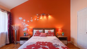 A bedroom with a large bed, two bedside tables, a nightstand, a wall-mounted light fixture, and a door.