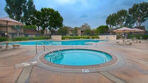 A swimming pool area with a hot tub, lounge chairs, and umbrellas.