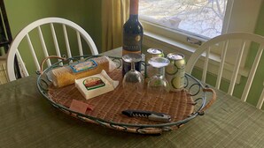 Una mesa de comedor con una bandeja de mimbre que contiene una botella de vino, queso, una lata de refresco y un cuchillo.