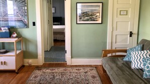 Una habitación con cama, escritorio con computadora, puerta y un cuadro en la pared.