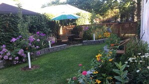 Un jardín bien cuidado con diversas flores, una valla de madera y una zona de patio con mobiliario exterior.