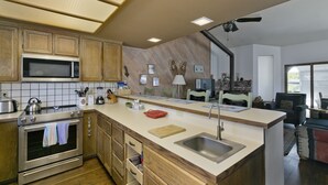 Een moderne keuken met houten kastjes, een magnetron, een spoelbak en een eethoek met een tafel en stoelen.