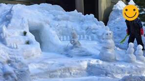 Snow sculptures adorn the grounds, featuring a snowman, a small snow figure, and a snowman with a shovel.
