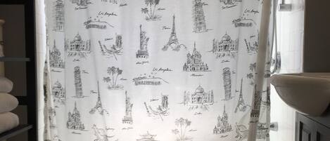 A bathroom with a shower curtain featuring city landmarks, a tiled floor, a toilet, and a shelf with towels.