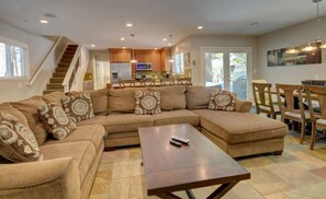 A spacious living room with a large sectional sofa, a wooden coffee table, and a dining area with wooden chairs.