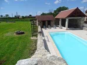 A swimming pool with a stone deck, a grassy lawn, and a stone building with a tiled roof. - GITE "ALBIZIA" and its swimming pool of 10x4 m. (Prissac)