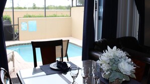Un comedor con una mesa dispuesta para dos, una piscina al fondo y vistas al exterior.