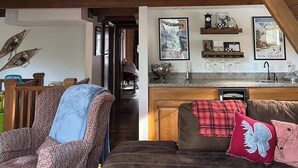 Un loft spacieux avec de hauts plafonds, des poutres apparentes, un coin salon confortable avec des tissus d’ameublement à motifs, et une cuisine dotée de plans de travail en granit et d’objets décoratifs.