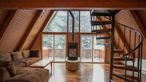 Une pièce mansardée chaleureuse avec une cheminée en pierre, un escalier en colimaçon et une grande fenêtre donnant sur une terrasse.