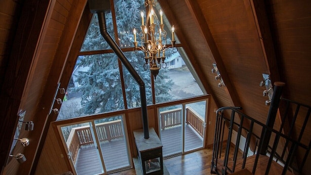 Une pièce en bois aux hauts plafonds, dotée d’une grande fenêtre, d’un lustre et d’une cheminée.