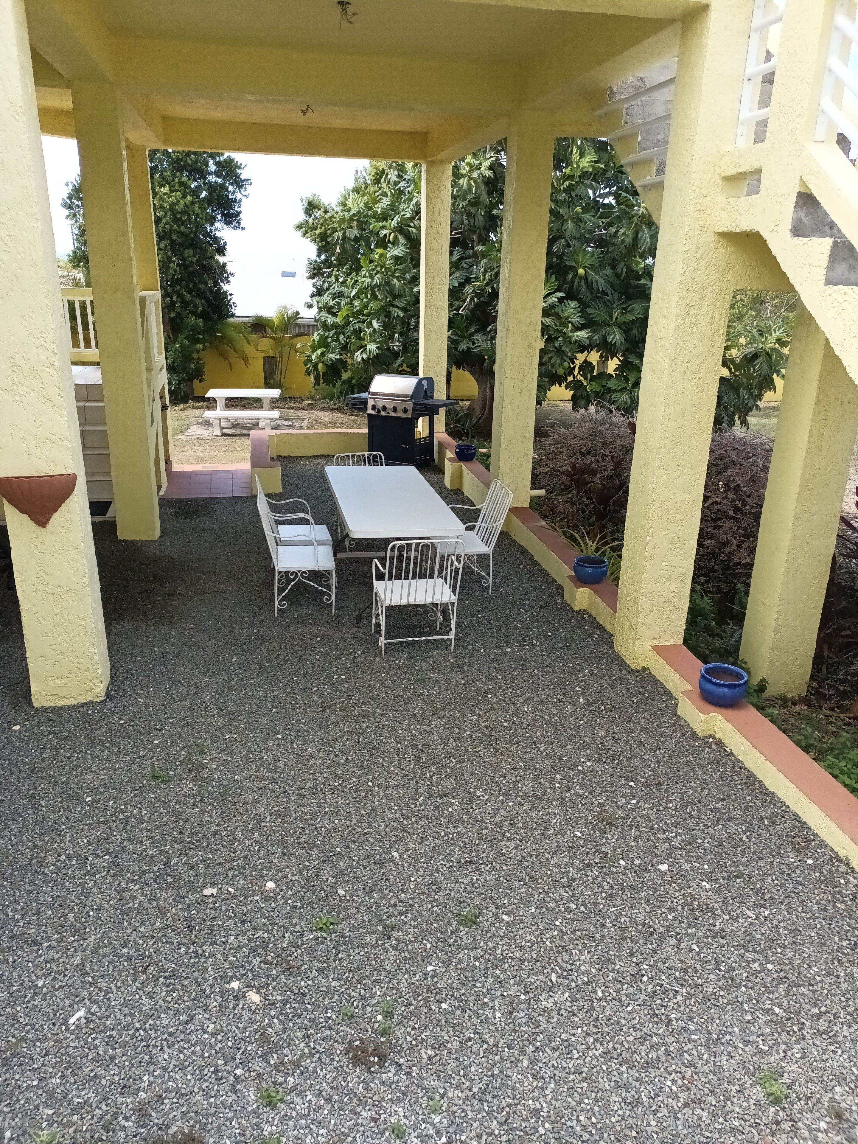 En uteplats med ett bord och stolar, en grill och en trappa som leder upp till en övre våning.