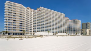 Ett stort hotell med flera våningar och en böjd fasad, beläget på en sandstrand under en klarblå himmel.