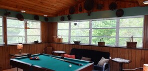 A pool table with balls, a sofa, and a window with a view of trees.