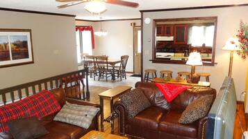 A living room with a brown leather sofa, a wooden coffee table, and a dining area with a wooden table and chairs.