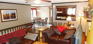 A living room with a brown leather sofa, a wooden coffee table, and a dining area with a wooden table and chairs.